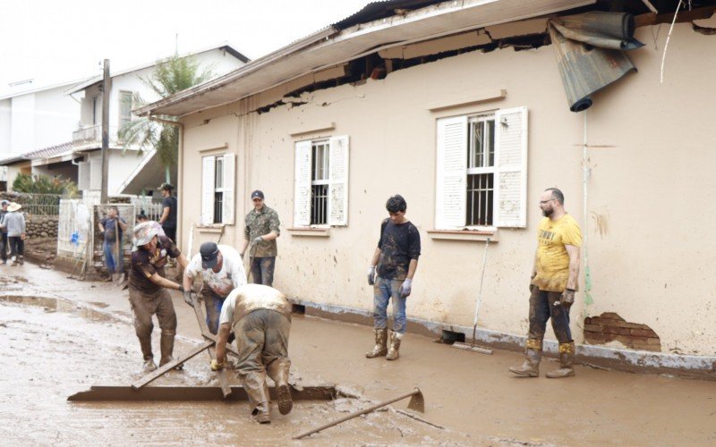 Grupo de Dois IrmÃ£os tentando remover excesso de lama em frente Ã  residÃªncia destruÃ­da pela enchente