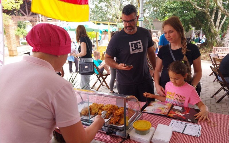 
Depois de Manuela Backes Dietrich de Ãvila, 6 anos, escolher seus livros, ela e seus pais, o corretor imobiliÃ¡rio Diego de Ãvila, 38 anos, e a funcionÃ¡ria pÃºblica Jaqueline Backes Dietrich, 37, compraram bolinhos de batata com linguiÃ§a de Roselei Michalski.
