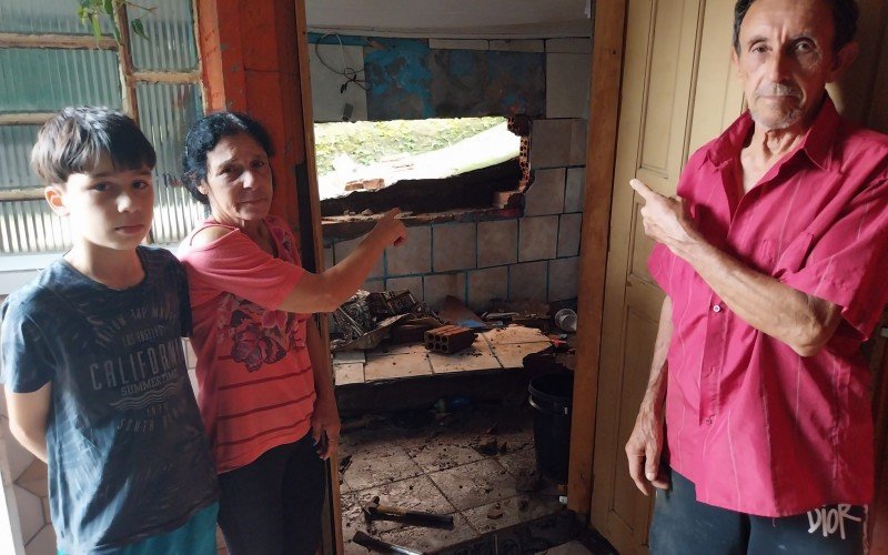 Idosos e neto mostram a cozinha cuja parede desabou com a  forÃ§a das Ã¡guas da tempestade 