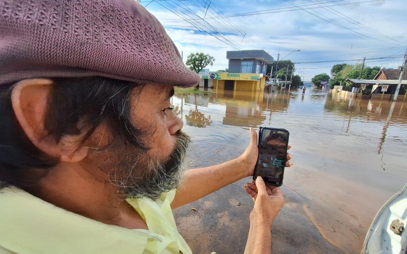 Vitor Mendes Ferreira mostra, no celular, foto aérea que indica que sua casa está coberta d'água | abc+