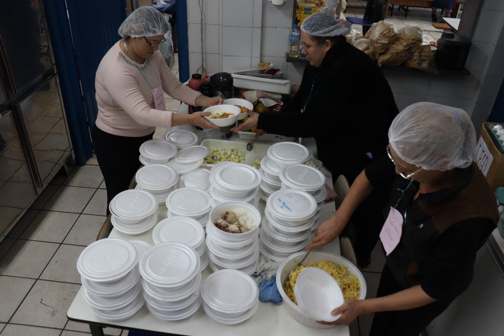 VoluntÃ¡rias da cozinha preparam marmitas para almoÃ§o de abrigados na Escola GusmÃ£o Britto