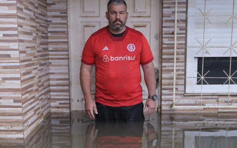 Alex Abel posou com orgulho em frente à sua casa tomada pela água, carregando na camiseta do time do coração as marcas da inundação