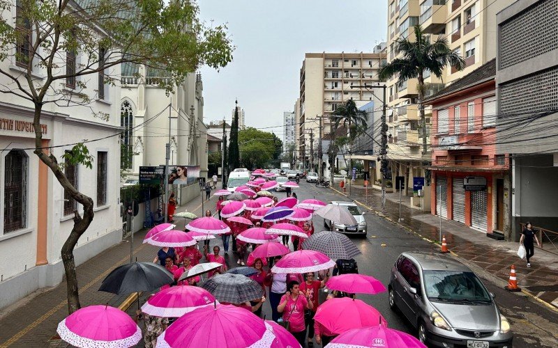 Com guarda-chuvas rosas, grupo Amigas de Mãos Dadas caminha pelo centro de Novo Hamburgo. | abc+