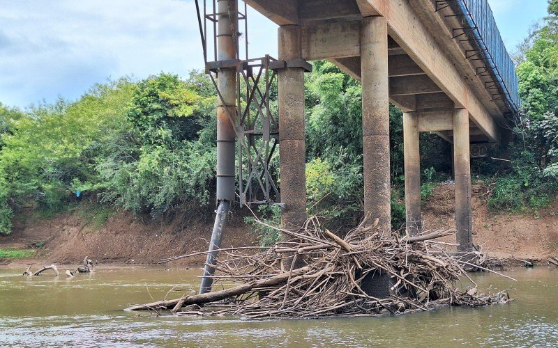 Com o nível baixo, o fundo do rio está exposto, revelando acúmulo de sujeira e troncos presos nos pilares da ponte na Barrinha, em Campo Bom