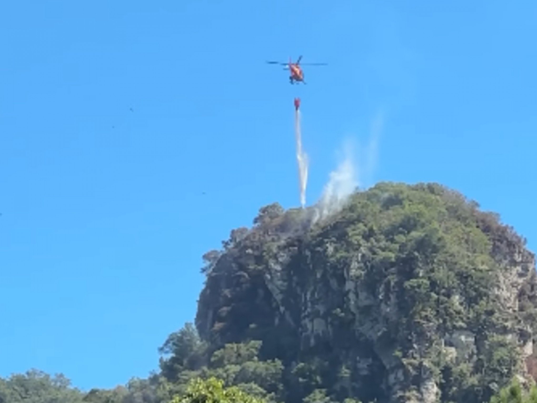 VÍDEO: Helicóptero usa helibalde para lançar água em foco de incêndio em morro na região metropolitana