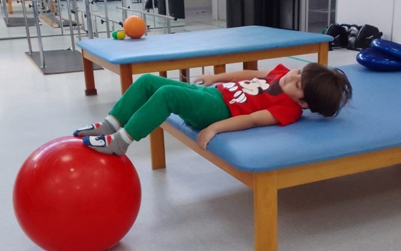 Menino passa por sessões de fisioterapia para enfrentar a doença