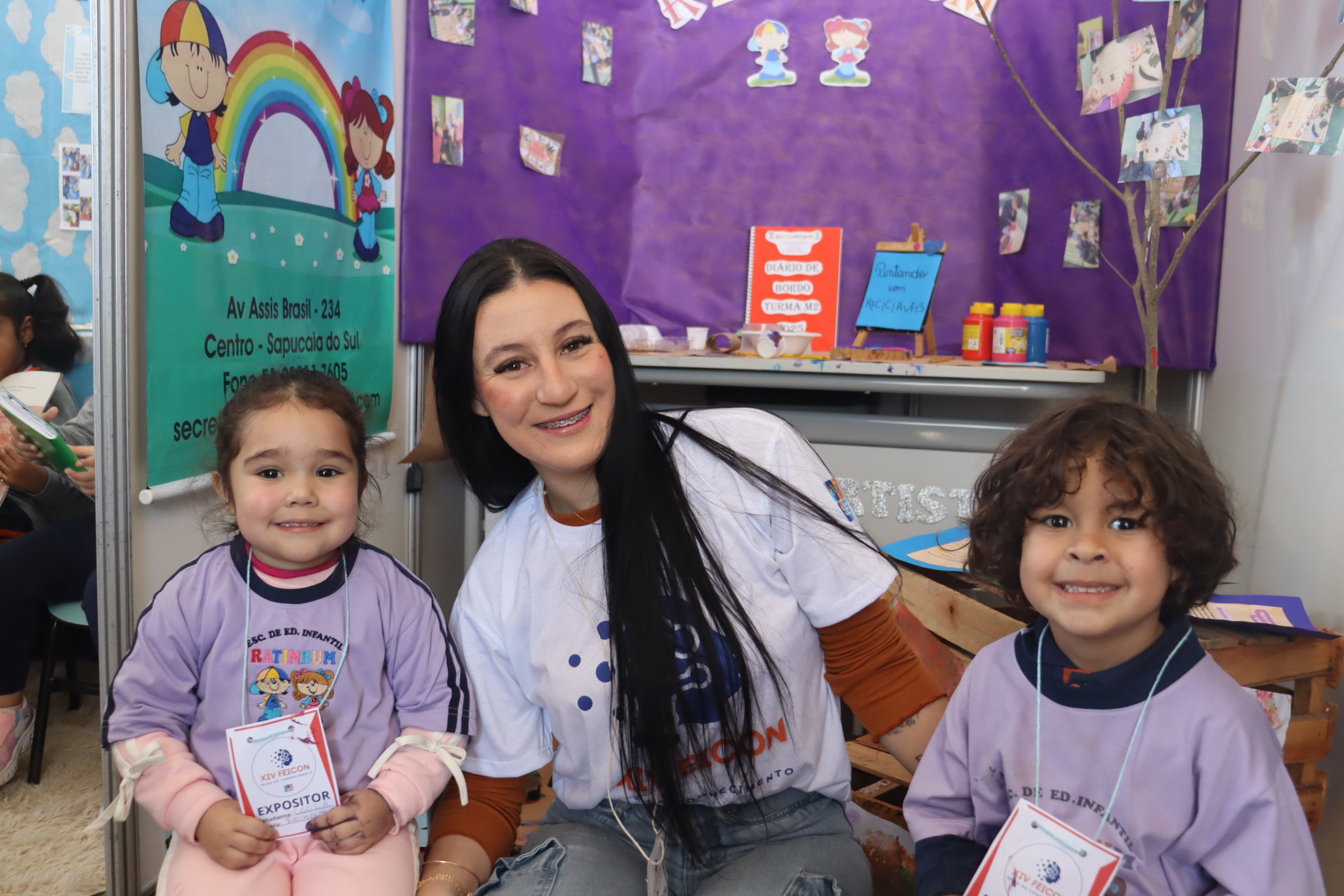 A Escola de Educação Infantil Rá Tim Bum participa da 14ª Feicon com o projeto Pintar com a Natureza. Na foto, a professora Eduarda Rohers (centro), posa com os alunos Cecília Lacerda e Joaquim Gonçalves